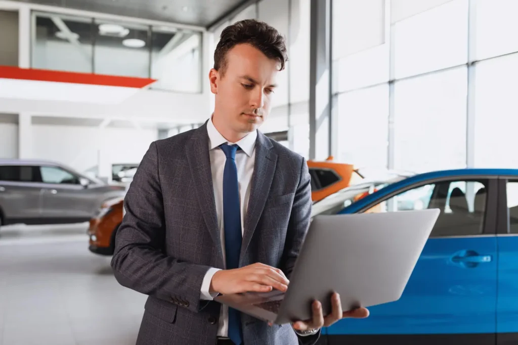 SEO Services for Automotive & Car Dealership – Drive Organic Leads 3 Dealership manager auditing a vehicle stock website on a laptop in a UK showroom